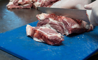 The butcher cuts a piece of pork in the kitchen with a sharp knife. A cook in white gloves is cutting meat.