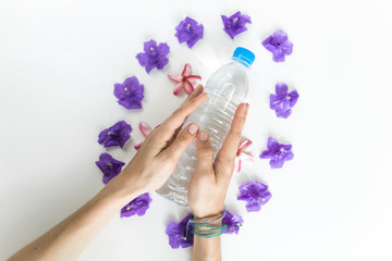 Plastic bottle of water on white background with woman hand, palm and flower