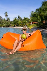 Young blonde man, boy at the beach with Lazy Inflatable Air Bed, hammock, couch camping.  Lounger Sofa Beach Chair Portable Sleeping Bag Mattress. Relax, vacation, travel. Coconut, sun glasses, hat