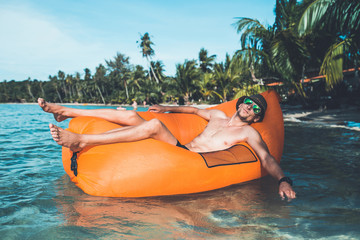 Young blonde man, boy at the beach with Lazy Inflatable Air Bed, hammock, couch camping.  Lounger Sofa Beach Chair Portable Sleeping Bag Mattress. Relax, vacation, travel. Asia. Thailand