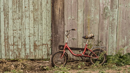 Fototapeta na wymiar an old children's bicycle is standing near a wooden fence