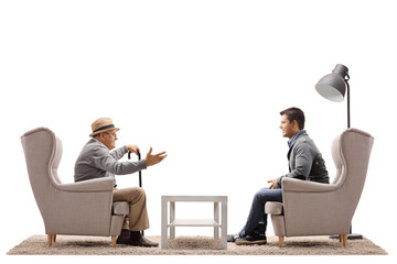 Elderly man and a young guy sitting in armchairs and having a conversation