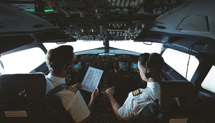 Pilot and copilot looking at instruction list in airplane
