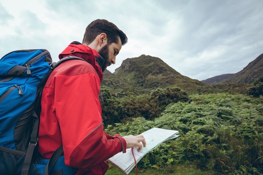 Male hiker reading the map near the green hills
