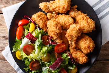 Crispy chicken wings in breadcrumbs and fresh salad close-up on a plate. horizontal top view