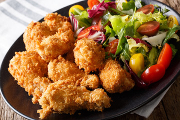 Spicy deep-fried chicken wings in breadcrumbs and fresh vegetable salad close-up. horizontal