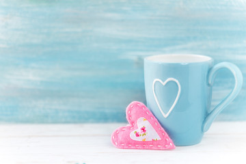 Valentine's day concept with pink handmade felt heart and a light blue cup against turquoise wooden background