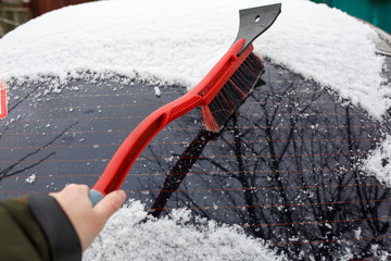 Man cleaning snow from car with brush