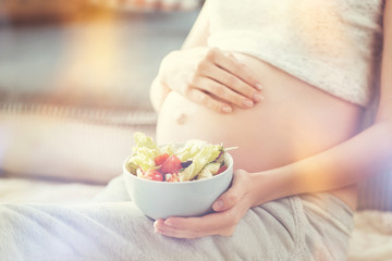 Obraz na płótnie Canvas Healthy diet. Close up of greek salad in hands of pleasant pregnant woman going to eat it and resting at home