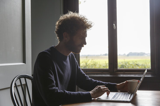 A man working on a laptop computer in the clean interior of a design country house in the netherlands.