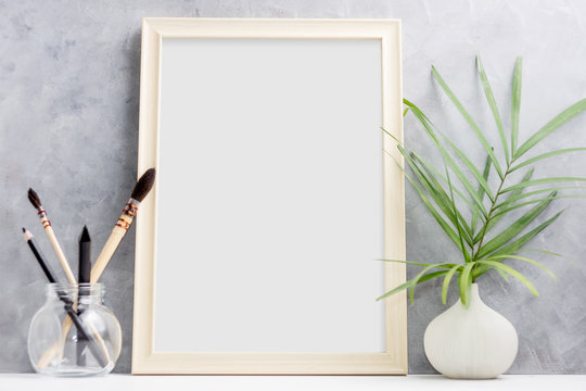 Large wooden Photo frame mock up with green palm leaves in vase and brushes in glass on shelf. Scandinavian style. Text space