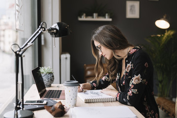 Woman drawing in sketch book at desk in tattoo studio