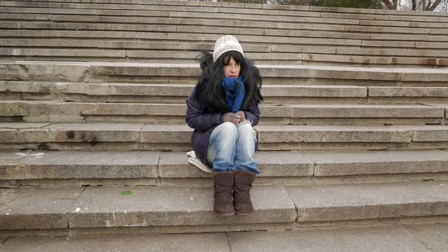 Hobo girl sitting at stairs and sad winter cold city
