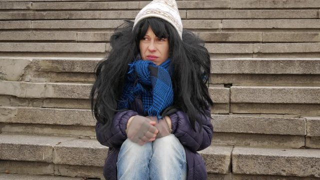 Homeless girl sitting at stairs and sad winter cold city
