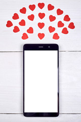 Close up of mobile smart phone with white blank screen and red paper hearts on wooden background, copy space. Flat lay, top view. Application mock up template for Saint Valentines Day