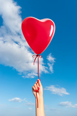 Fototapeta na wymiar Womans hand with heart shaped balloon on background of sky.