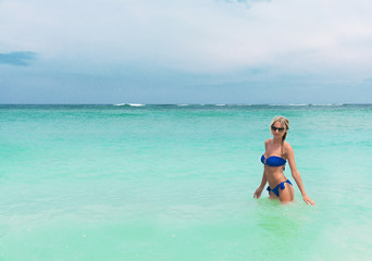 Young pretty blond woman in blue bikini on white tropic beach