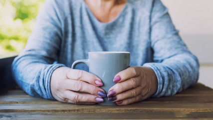 Hands of an elderly woman holding a cup of hot tea