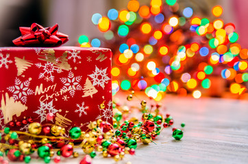 Christmas present with a small red bow on the background of multi-colored Christmas lights.
