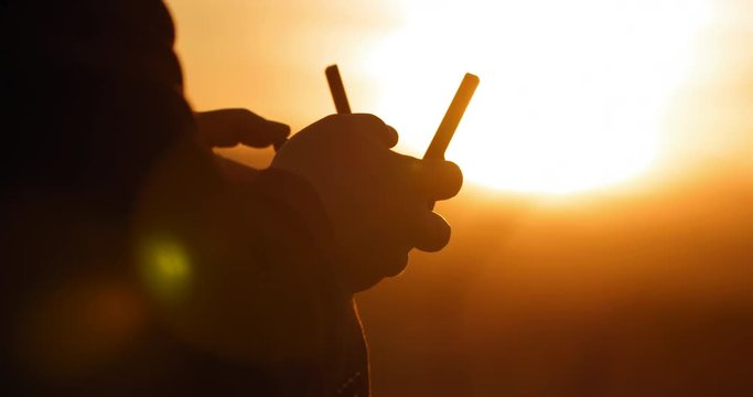 Close view of pilot's hands with remote control as he flies a drone at sunset. Strongly backlit with silhouette and lens flares. Hand-held real-time 4K.