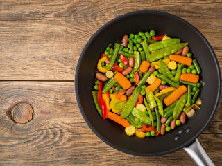 big pan fried with colorful vegetables - peppers, peas, green beans, baby corn, carrots, beans. Colorful vegetarian lunch, top view, wooden background, space for text