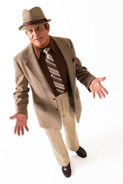 Older Man in Fine Brown Suit and Hat on White Background Palms Up. An older gentleman in a fine brown suit and hat in front of a plain, white background, gesturing.