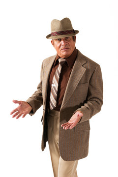 Older Man in Fine Brown Suit and Hat on White Background Gesturing. An older gentleman gesturing in a fine brown suit and hat in front of a plain, white background.