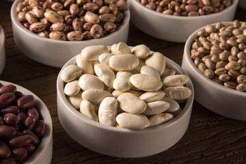 Assorted beans in bowls on wood background