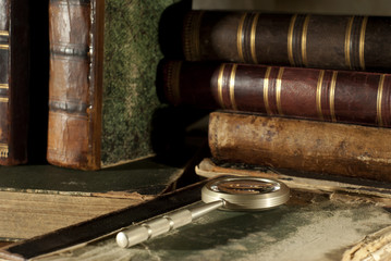 An ancient book in a ragged cover and a magnifying glass on a table closeup on a blurred background of other old books