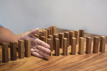 Risk and strategy in business, Close up of businessman hand stopping wooden block between three way from falling in the line of domino