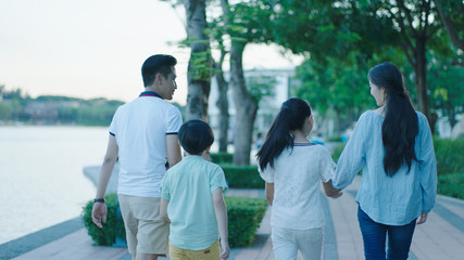 Rear view of Asian family smiling & walking on waterfront promenade at dusk © allensima