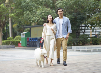 Asian couple laughing while walking dog outdoor in garden