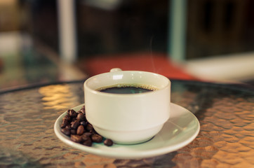 Hot American coffee in a white coffee mug and coffee beans around a coffee mug.Vintage tone