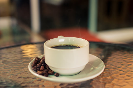 Hot American coffee in a white coffee mug and coffee beans around a coffee mug.Vintage tone