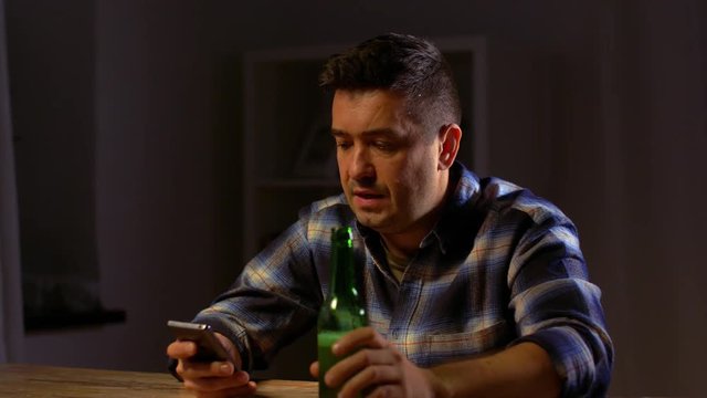 man with smartphone drinking bottled beer at home