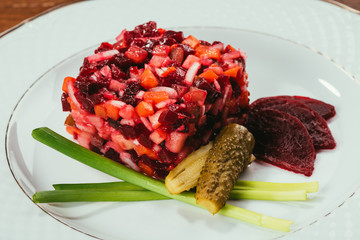 Close-up view of Vinegret salad served with green onion and pickled cucumber on white plate
