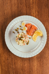 Russian salad on plate with scattered peas, boiled eggs and fish slices