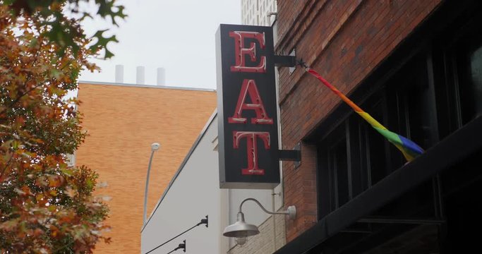A daytime view of a red neon "EAT" sign on the side of a restaurant in a large city. Day/night matching available.  	