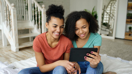 Fototapeta premium Cheerful mixed race young funny girls talking online video chat on tablet computer with their friends at home