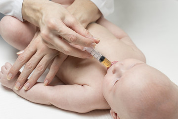 One caucasian female doctor is giving some dose of liquid medicine to infant baby boy by syringe into the mouth from disease or for vaccination