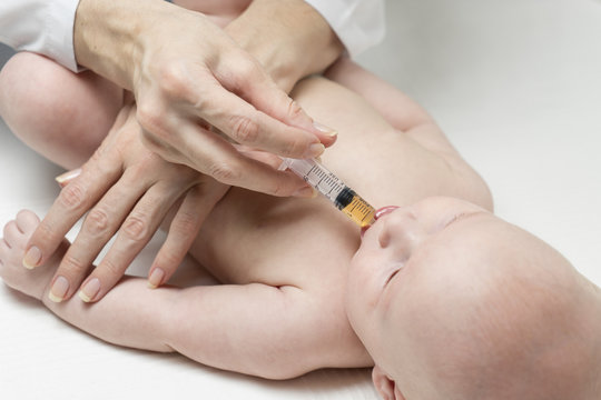 One caucasian female doctor is giving some dose of liquid medicine to infant baby boy by syringe into the mouth from disease or for vaccination