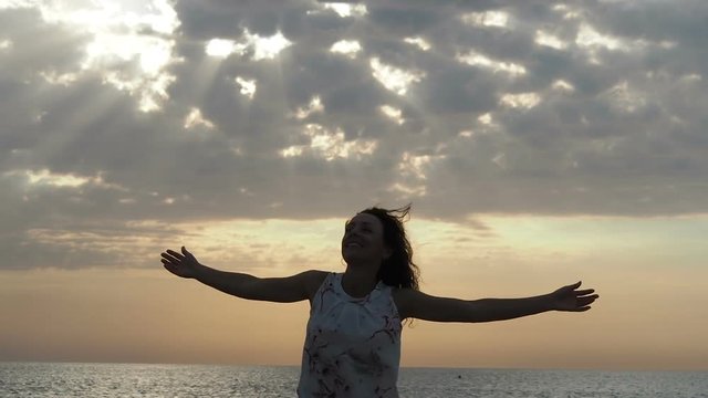 Sun rays through the clouds. A happy woman is spinning with arms outstretched against the rays of the sun over the sea.