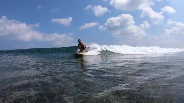 Surfer rides crystal clear ocean wave at sunny day and shows the Shaka sign