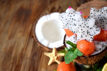 Tropical fruits. Papaya balls, coconuts, limes and pitahaya carved stars on a wooden table