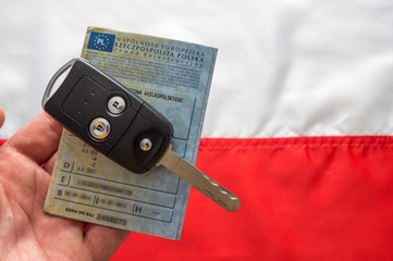 Dowód rejestracyjny i kluczyki do samochodu na tle flagi Polski.
