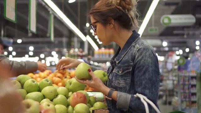 Young woman chooses fruit apples in a store