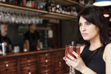 Bella ragazza con i capelli neri che tiene un bicchiere e guarda seria nello sfondo - sfondo bar