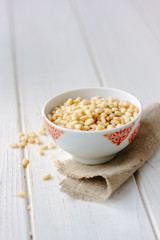 Pine nuts in a ceramic bowl over wooden table.