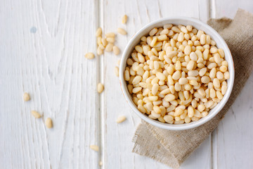 Pine nuts in a ceramic bowl over wooden table.