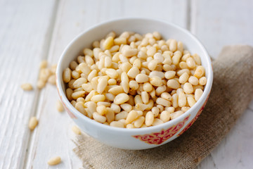 Pine nuts in a ceramic bowl over wooden table.